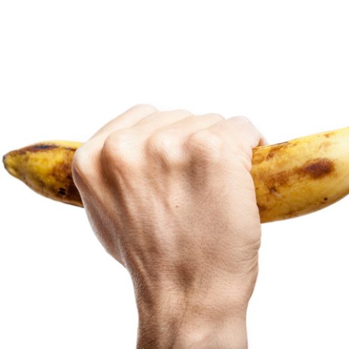 Hand man squeezes a ripe banana on a white background